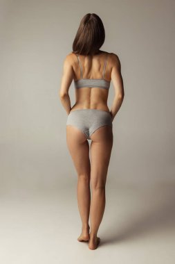 Gri stüdyo arka planında izole edilmiş iç çamaşırlı güzel, zayıf bir kadının portresi. Doğal güzellik konsepti. Arka plan