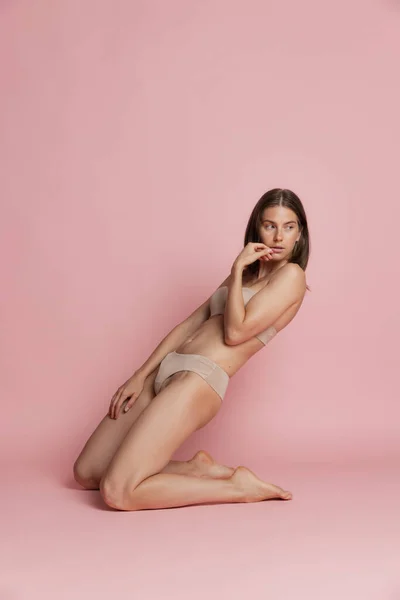 Portret van jonge mooie gebruinde vrouw in lingerie poseren geïsoleerd over roze studio achtergrond. Natuurlijke schoonheid concept. — Stockfoto