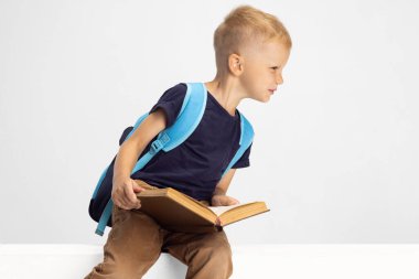 Anaokulundan bir çocuk beyaz stüdyo arka planında izole edilmiş bir şekilde oturup kitap okuyor. Reklam için kopyalama alanı. Çocukluk, eğitim, duygu konsepti