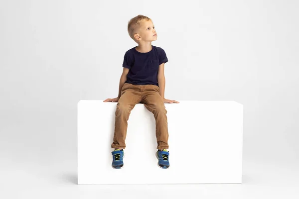 Один дошкольник, сидящий на большой коробке, изолированный на белом фоне студии. Копировальное пространство для рекламы. Детство, образование, эмоциональная концепция — стоковое фото