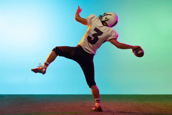 Portret van American football speler training geïsoleerd op blauwe studio achtergrond in neon licht. Begrip sport, concurrentie — Stockfoto