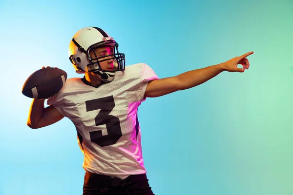 Retrato de entrenamiento de jugador de fútbol americano aislado en fondo de estudio azul en luz de neón. Concepto de deporte, competición — Foto de Stock