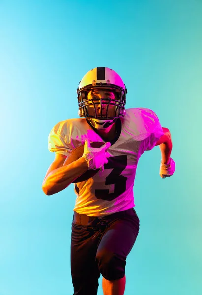 Close-up mannelijke American football speler training geïsoleerd op blauwe studio achtergrond in neon licht. Begrip sport, concurrentie — Stockfoto