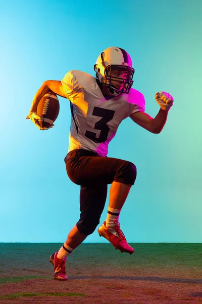 Portrait of American football player training isolated on blue studio background in neon light. Concept of sport, competition