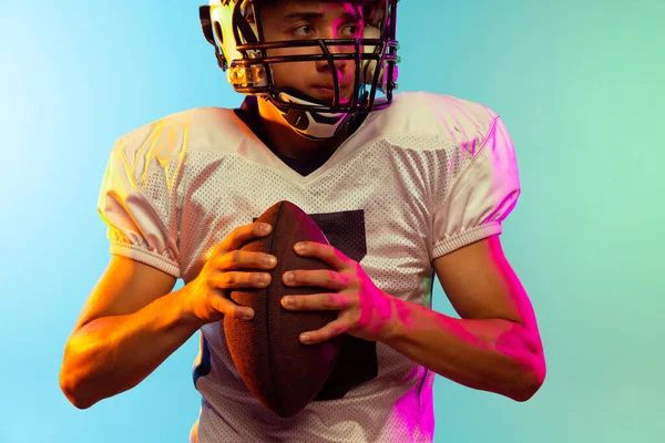 Nahaufnahme eines männlichen American-Football-Spielers, der isoliert auf blauem Studiohintergrund im Neonlicht trainiert. Konzept Sport, Wettbewerb — Stockfoto