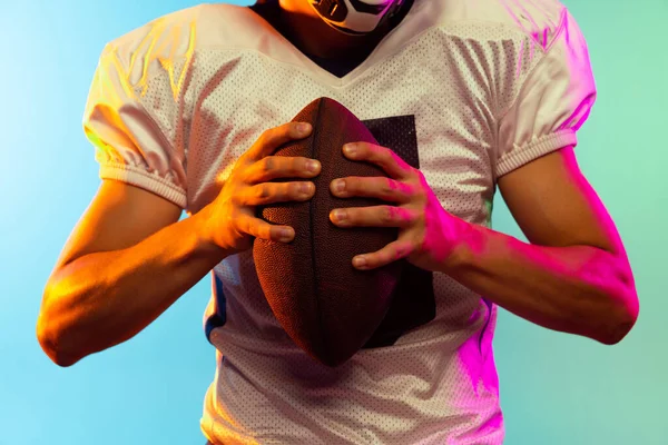 Imagem cortada de jogador de futebol americano masculino isolado no fundo do estúdio azul em luz de néon. Conceito de desporto, competição — Fotografia de Stock