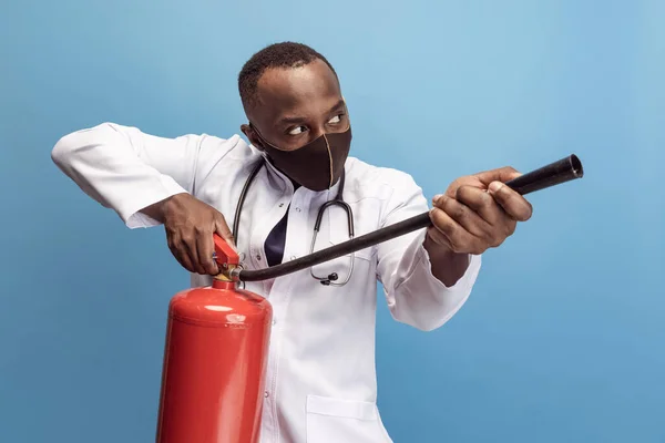 Porträt eines jungen Mannes, Arztes, Therapeuten oder medizinischen Beraters mit Feuerlöscher isoliert auf blauem Hintergrund. Lustige Meme. — Stockfoto