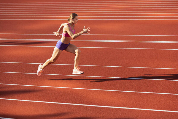 One Caucasian woman, female athlete, runner training at public stadium, sport court or palyground outdoors. Summer sport games.