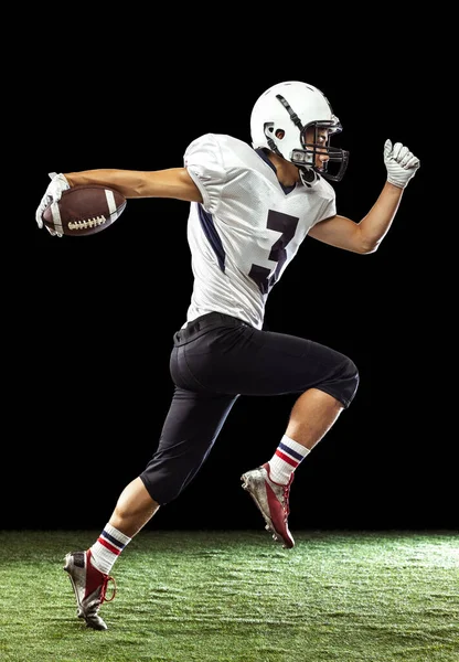 Portret van American football speler training geïsoleerd op donkere studio achtergrond met gras vloeren. Begrip sport, concurrentie, doelstellingen, prestaties — Stockfoto