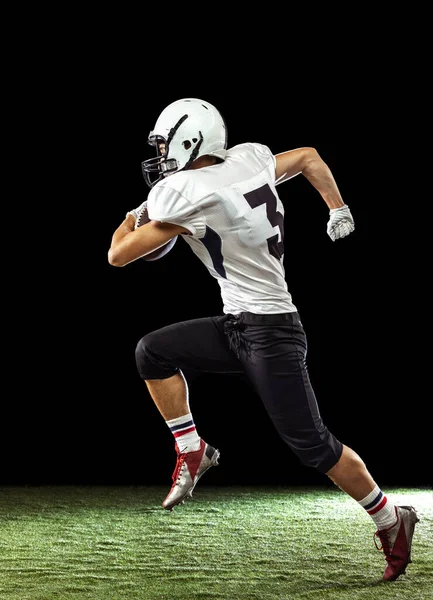 Portrait of American football player training isolated on dark studio background with grass flooring. Concept of sport, competition, goals, achievements — Stock Photo, Image