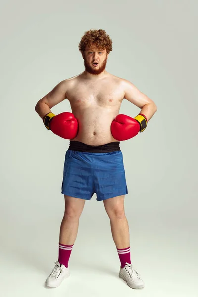 Homme roux drôle en short de boxe bleu et gants isolés sur fond de studio gris. Concept de sport, humour et corps positif. — Photo