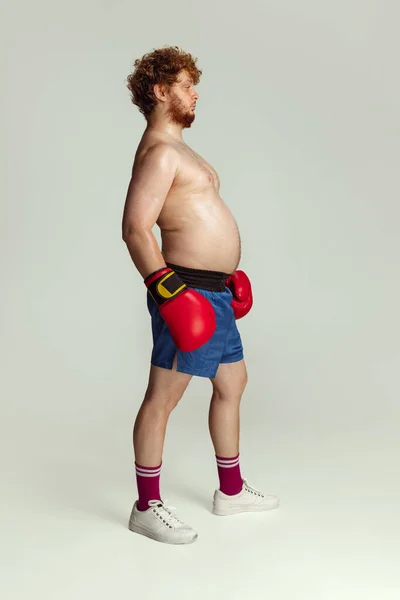 Homme roux drôle en short de boxe bleu et gants isolés sur fond de studio gris. Concept de sport, humour et corps positif. — Photo