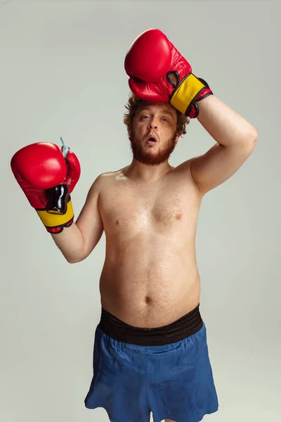 Homme roux drôle en short de boxe bleu et gants isolés sur fond de studio gris. Concept de sport, humour et corps positif. — Photo