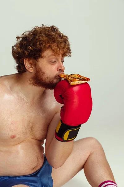 Divertente uomo dalla testa rossa in pantaloncini da boxe blu e guanti isolati su sfondo grigio studio. Concetto di sport, umorismo e corpo positivo. — Foto Stock