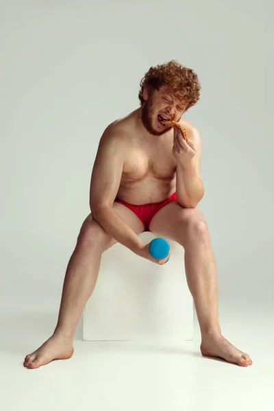 Homem ruivo bonito em shorts de natação vermelho posando isolado no fundo do estúdio cinza. Conceito de esporte, humor e corpo positivo. — Fotografia de Stock