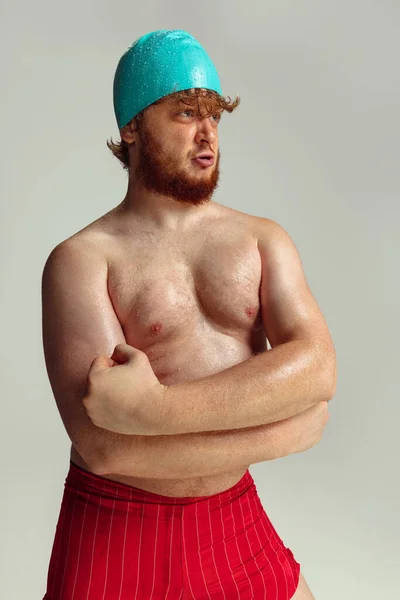 재미있는 수영 선수. 빨간 머리의 빨간 수영복을 입고 회색 스튜디오 배경에 고립된 채누워 있는 귀여운 붉은 머리의 남자. 스 포오 츠 , 유우머 및 신체적 양성 개념. — 스톡 사진