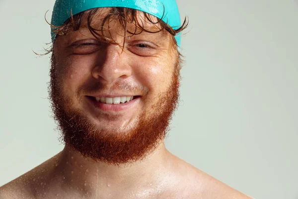 Close-up image of red-headed man in swimming hat posing isolated on gray studio background. Concept of sport, humor and body positive. — Stock Photo, Image