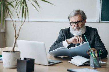 Yaşlı, kır saçlı bir adam, profesör, iş yerinde çalışan bir öğretmen, içeride. Meslek mesleği, iş, eğitim ve motivasyon kavramı.