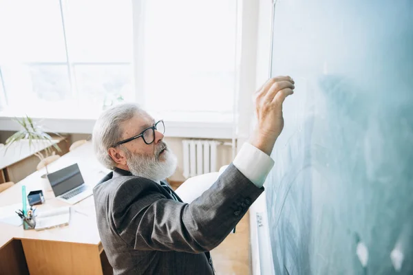 High angle view of elderly gray-headed man, professor, teacher at lecture, lesson at classroom, indoors. Concept of professional occupation, job, education