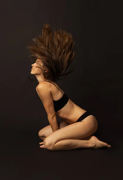 Retrato de jovem bela mulher bronzeada magro em lingerie preta posando isolado sobre fundo estúdio escuro. Beleza natural, bem-estar, conceito de estilo de vida saudável. — Fotografia de Stock