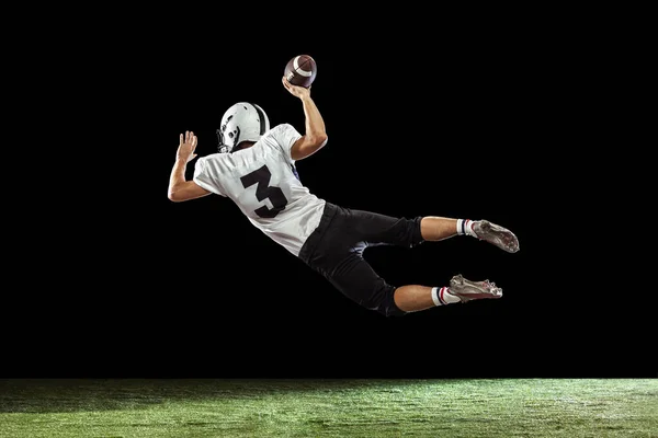 Portrait of American football player training isolated on dark studio background with green grass flooring. Concept of sport, competition — Stock Photo, Image