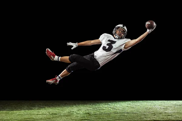 Portret van American football speler training geïsoleerd op donkere studio achtergrond met groen gras vloeren. Begrip sport, concurrentie — Stockfoto