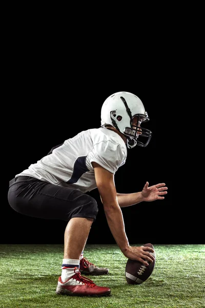 Portret van American football speler training geïsoleerd op donkere studio achtergrond met gras vloeren. Begrip sport, concurrentie, doelstellingen, prestaties — Stockfoto