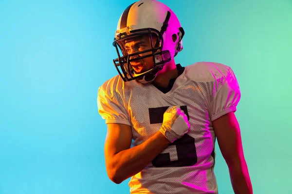 Retrato de um jogador de futebol americano em equipamento esportivo capacete e luvas isoladas em fundo estúdio azul em luz de néon. Conceito de desporto, competição — Fotografia de Stock