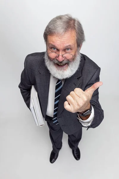 Hochwinkelaufnahme eines älteren grauhaarigen Mannes, Professors, Lehrers, der isoliert auf grauem Studiohintergrund posiert. Konzept von Beruf, Beruf, Ausbildung und Motivation. — Stockfoto