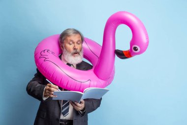 Mavi stüdyo arka planında yalnız çalışan yaşlı, gri saçlı bir adam, profesör ve öğretmenin portresi. Meslek mesleği, iş, eğitim ve motivasyon kavramı.