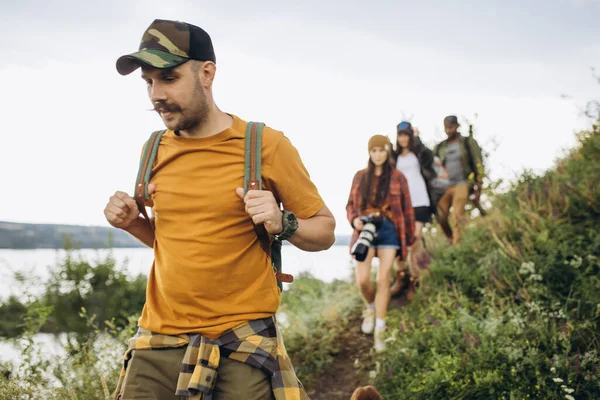 Pięciu młodych przyjaciół, młodych mężczyzn i kobiet spacerujących razem na obrzeżach miasta, w letnim lesie, na łące. Aktywny styl życia, przyjaźń, opieka, koncepcja ekologii — Zdjęcie stockowe