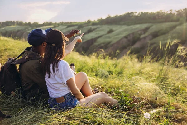 Voorgrond jonge man en vrouw, familie koppel zitten samen in weide, veld en genieten van de natuur. Actieve levensstijl, reizen, relatie, ontmoetingsconcept — Stockfoto