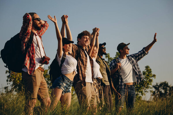 Meet sunset. Group of friends, young men and women walking, strolling together in summer forest, meadow outdoors. Active lifestyle, friendship