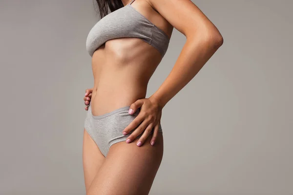 Hermoso cuerpo de joven mujer caucásica en lencería gris aislada sobre fondo gris estudio. Concepto de belleza natural. Vista inferior — Foto de Stock