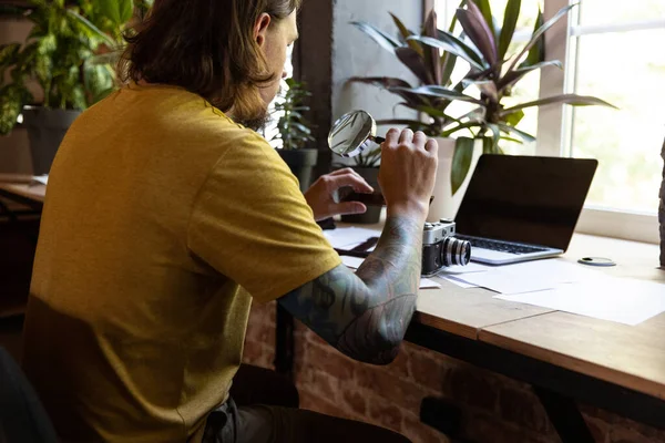 Un joven hombre caucásico, fotógrafo, camarógrafo con cámara profesional, equipo durante el trabajo en la oficina, en el interior. Concepto de ocupación, trabajo, educación — Foto de Stock