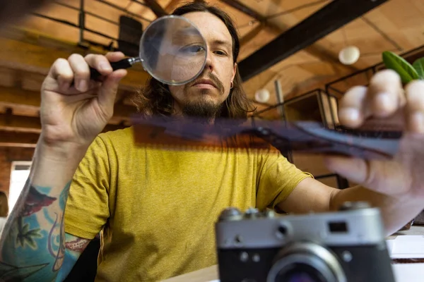 Un joven hombre caucásico, fotógrafo, camarógrafo con cámara profesional, equipo durante el trabajo en la oficina, en el interior. Concepto de ocupación, trabajo, educación —  Fotos de Stock