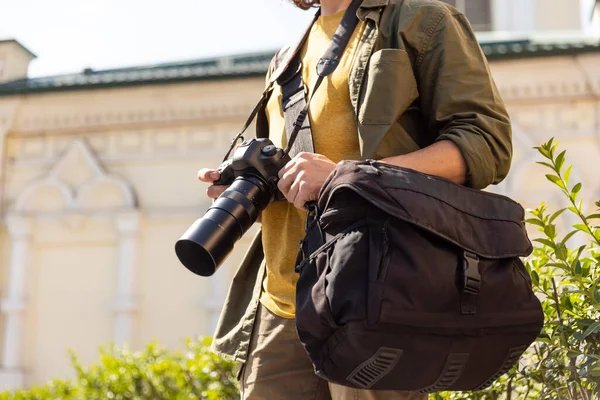 Portrait of young man, photographer, cameraman with professional camera, equipment during working summer day outdoors. Concept of occupation, job, education