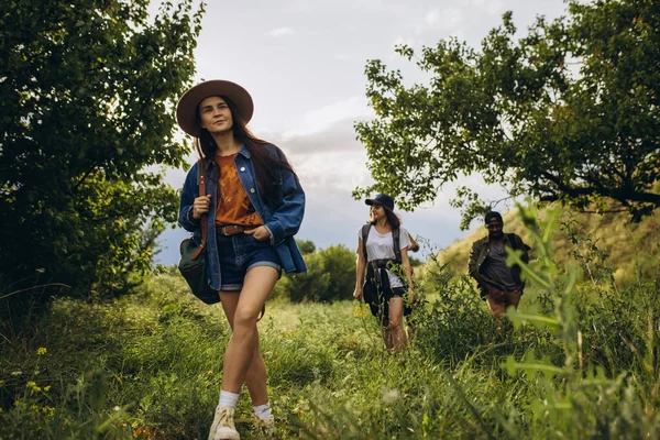 Groupe d'amis, jeunes hommes et femmes marchant, se promenant ensemble en périphérie de la ville, dans la forêt d'été, prairie. Style de vie actif, amitié, soins, concept écologique — Photo