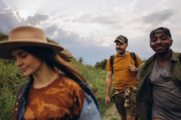 Group of friends, young men and women walking, strolling together outskirts of city, in summer forest, meadow. Active lifestyle, friendship, care, ecology concept — Stock Photo, Image