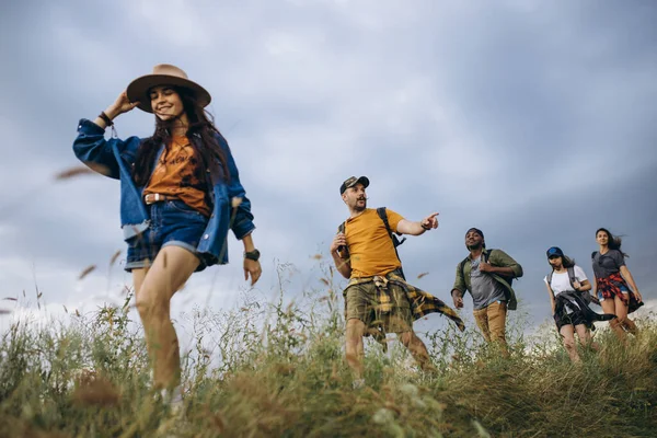 Groupe d'amis, jeunes hommes et femmes marchant, se promenant ensemble en périphérie de la ville, dans la forêt d'été, prairie. Style de vie actif, amitié, soins, concept écologique — Photo