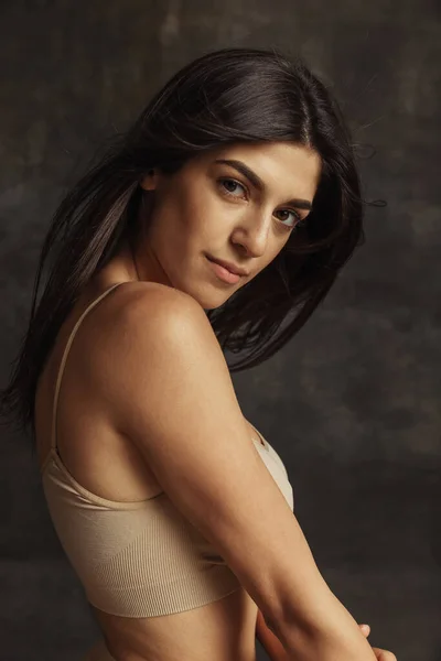 Retrato de una joven hermosa mujer bronceada en lencería posando aislada sobre un oscuro fondo de estudio vintage. Concepto de belleza natural. — Foto de Stock