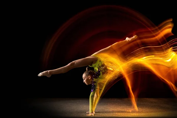 Portret młodej dziewczyny, artystka gimnastyki rytmicznej w akcji odizolowana na ciemnym tle pracowni z mieszanym światłem. Pojęcie sportu, działania, aspiracji, piękna — Zdjęcie stockowe