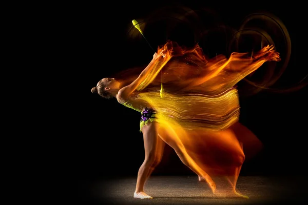 Porträtt av ung flicka, rytmisk gymnastik artist i aktion isolerad på mörk studio bakgrund med blandat ljus. Begreppet idrott, handling, strävan, skönhet — Stockfoto