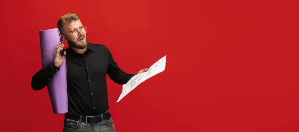 Портрет смішного бородатого чоловіка, будівельника, дизайнера або архітектора з професійним обладнанням ізольовано на червоному фоні студії . — стокове фото