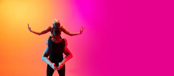 Két táncos, stílusos sportoló pár, férfi és női modellek táncolnak kortárs tánc színes gradiens sárga rózsaszín háttér neon fény. — Stock Fotó