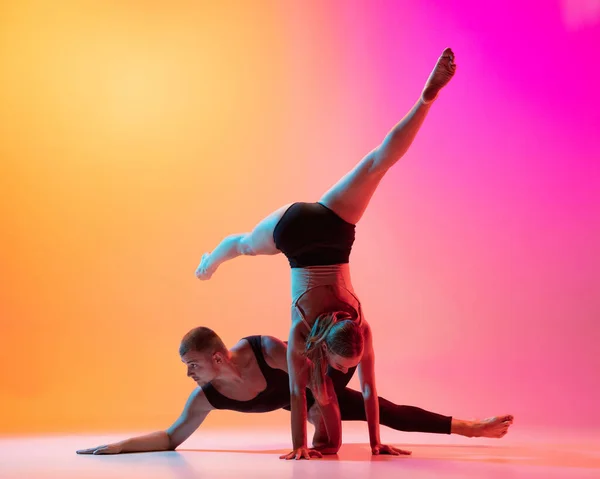 Deux danseurs, couple sportif élégant, mannequins hommes et femmes dansant la danse contemporaine sur fond rose jaune dégradé coloré au néon. — Photo