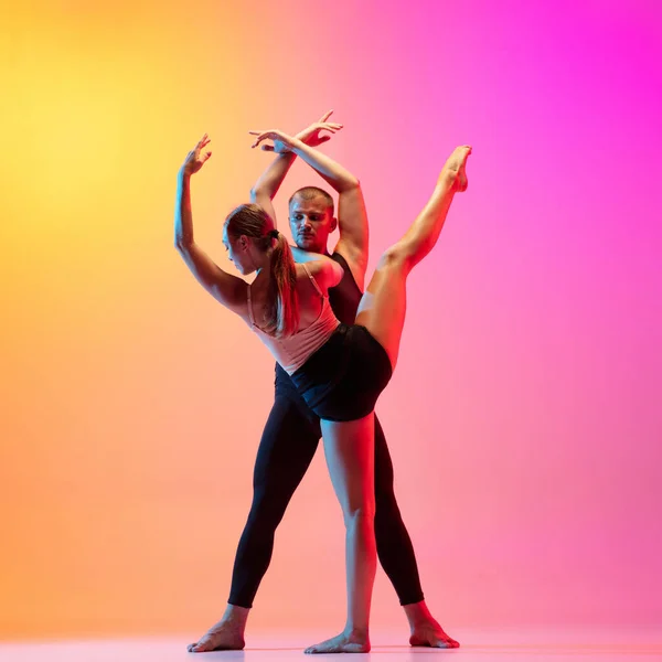 Два танцора, стильная спортивная пара, мужские и женские модели танцуют современный танец на ярко-желтом розовом фоне в неоновом свете. — стоковое фото