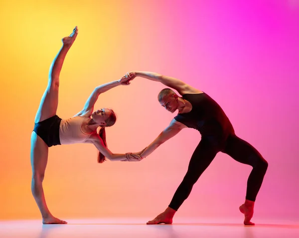 Dos bailarines, elegante pareja deportiva, modelos masculinos y femeninos bailando danza contemporánea sobre colorido degradado amarillo rosa fondo en luz de neón. — Foto de Stock