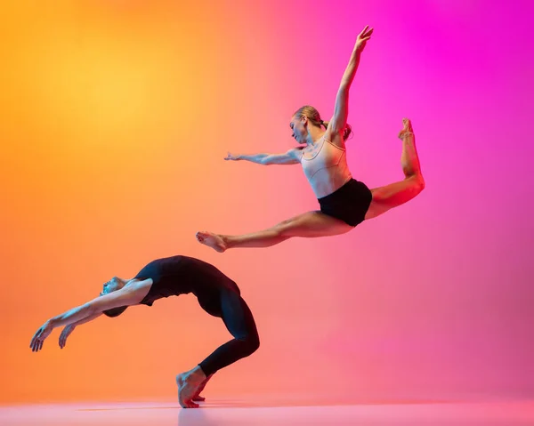 Dos bailarines, elegante pareja deportiva, modelos masculinos y femeninos bailando danza contemporánea sobre colorido degradado amarillo rosa fondo en luz de neón. — Foto de Stock