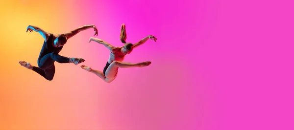 Twee dansers, stijlvol sportief koppel, mannelijke en vrouwelijke modellen dansen hedendaagse dans op kleurrijke gradiënt geel roze achtergrond in neon licht. — Stockfoto